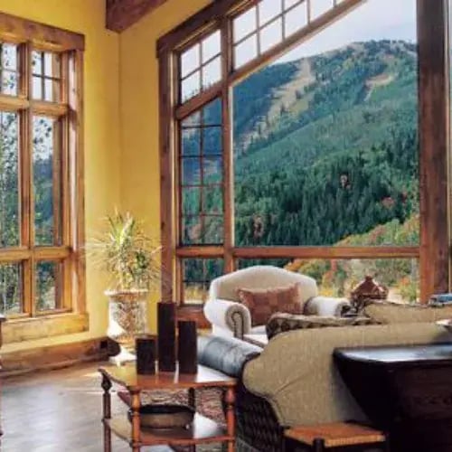 Tall wood-framed windows overlooking a wooded mountain landscape
